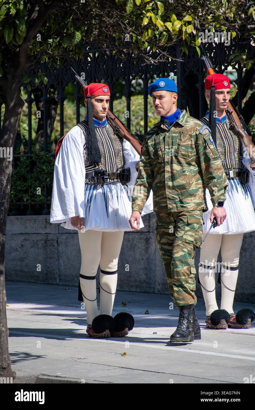 Due Evzoni in uniforme greca tradizionale marciano in formazione accanto a un soldato in mimetica moderna e un berretto blu. Foto Stock