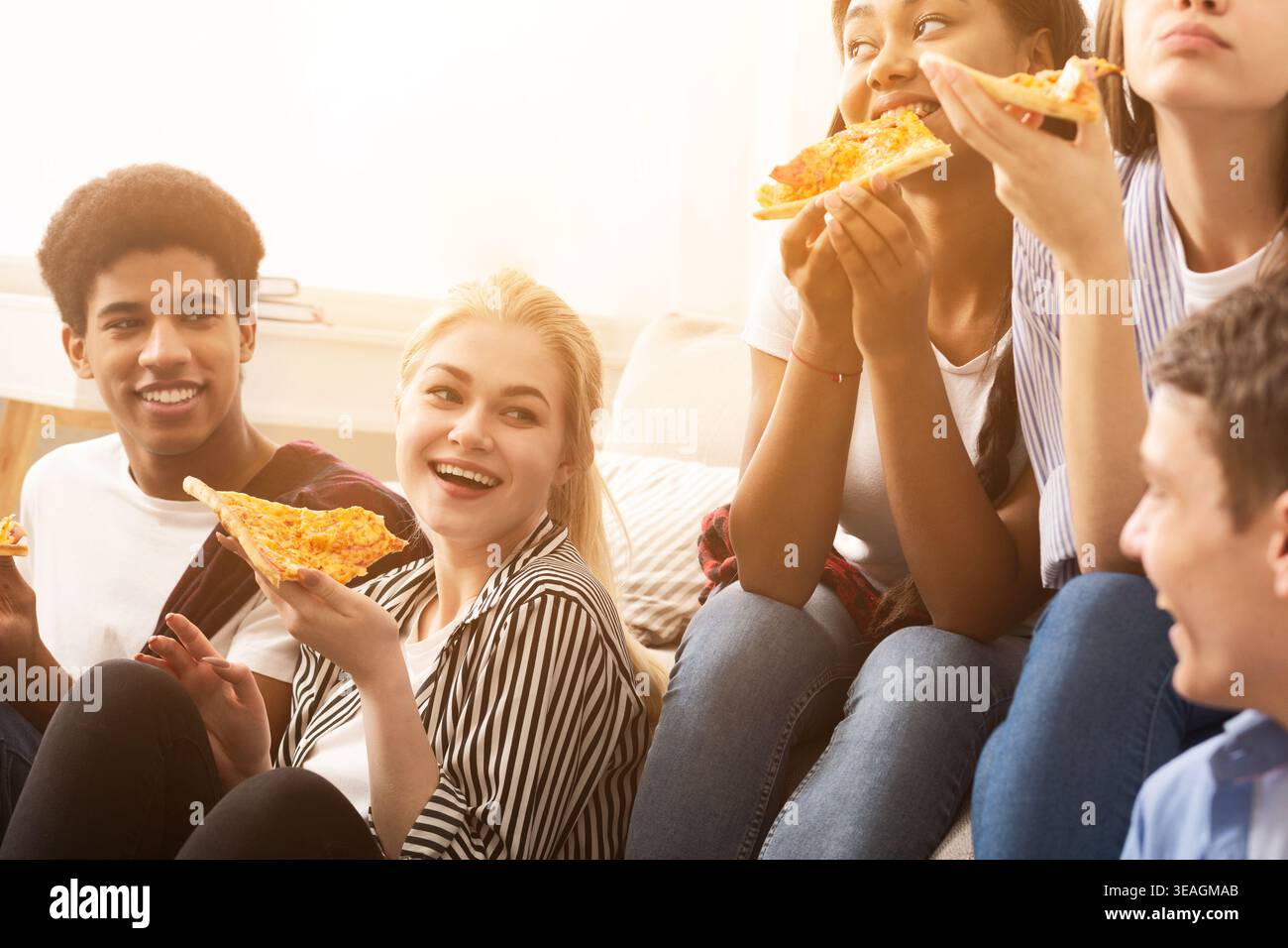 Gruppi di amici che si godono la pizza insieme mentre si siedono su un divano durante una riunione informale Foto Stock