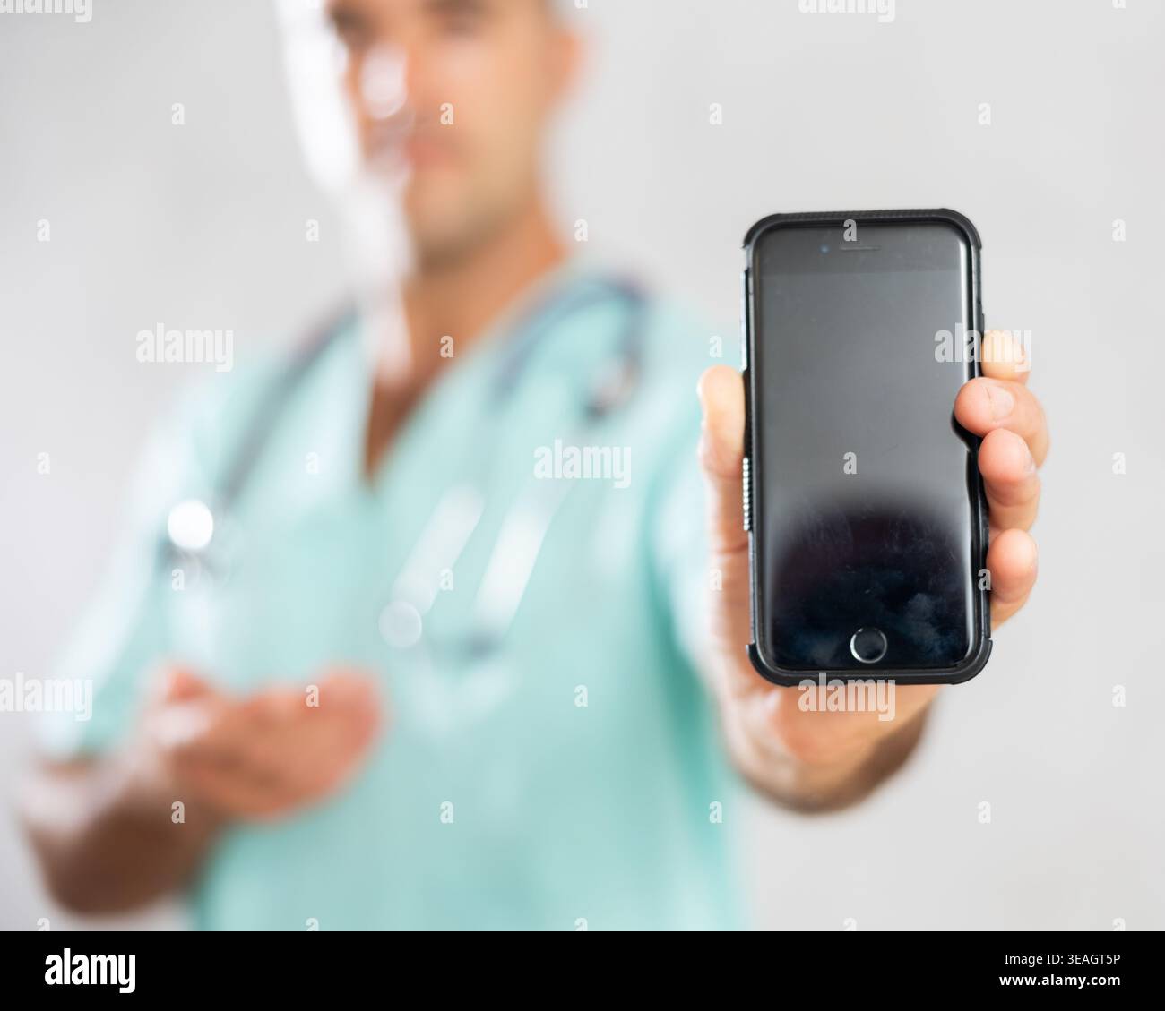Medico di sesso maschile in uniforme medica in posa con il telefono cellulare nella stanza medica Foto Stock