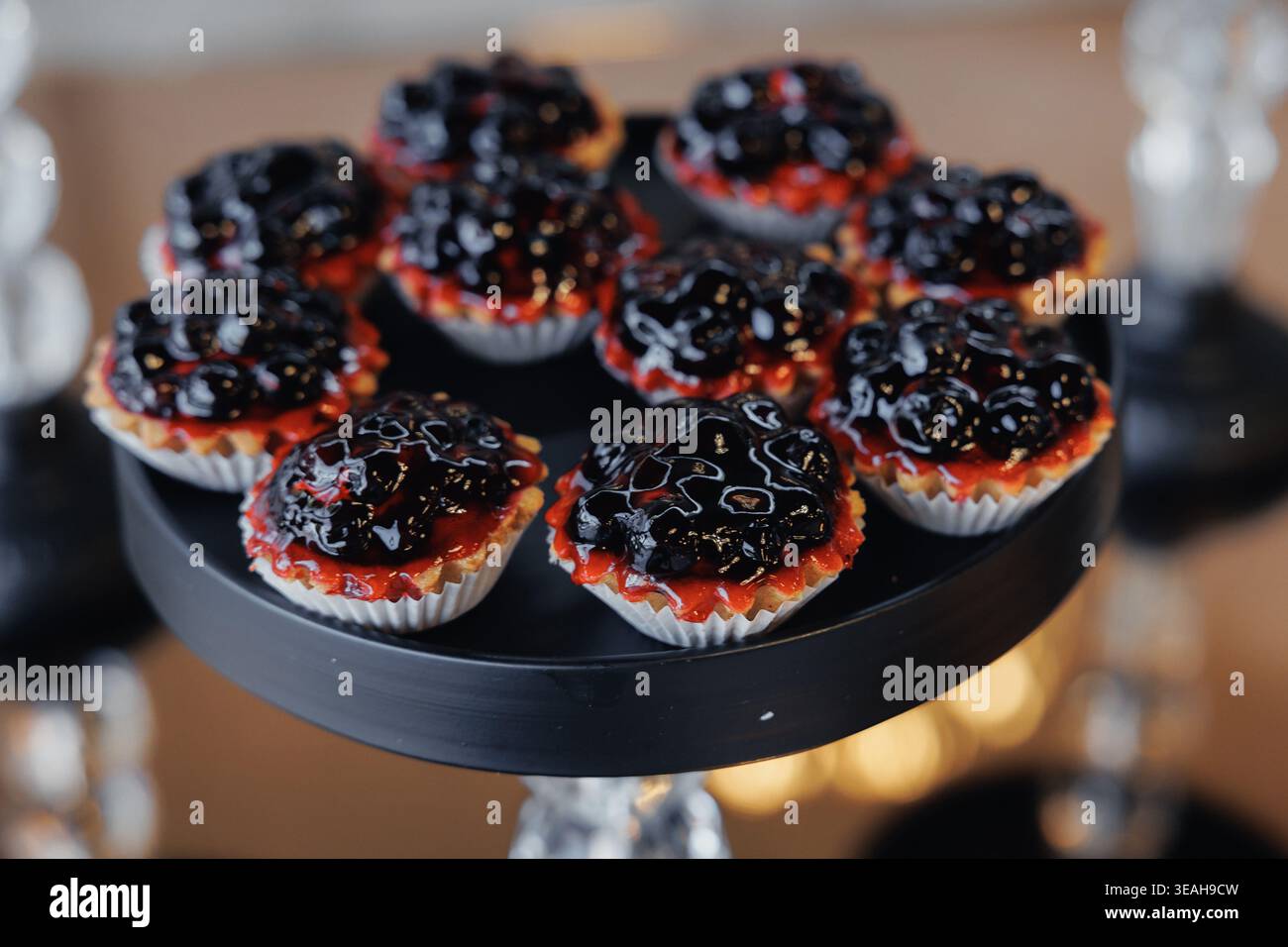 Berry Tarts on Black Stand, brunch stagionale con rivestimento in marmellata di mirtilli e glassa lucida, crosta in crosta di burro in fodera di carta, porzioni bitesizzate Foto Stock