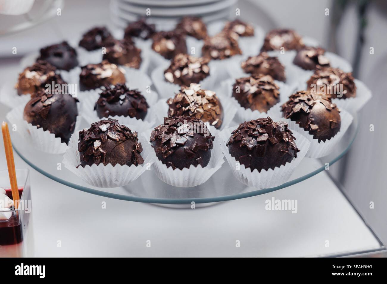 Tartufi di cioccolato fondente su piastra di vetro, grappoli di cacao ricchi ricoperti di goccioline bianche in tazze di carta, texture decadente e finitura lucida, realizzati a mano Foto Stock