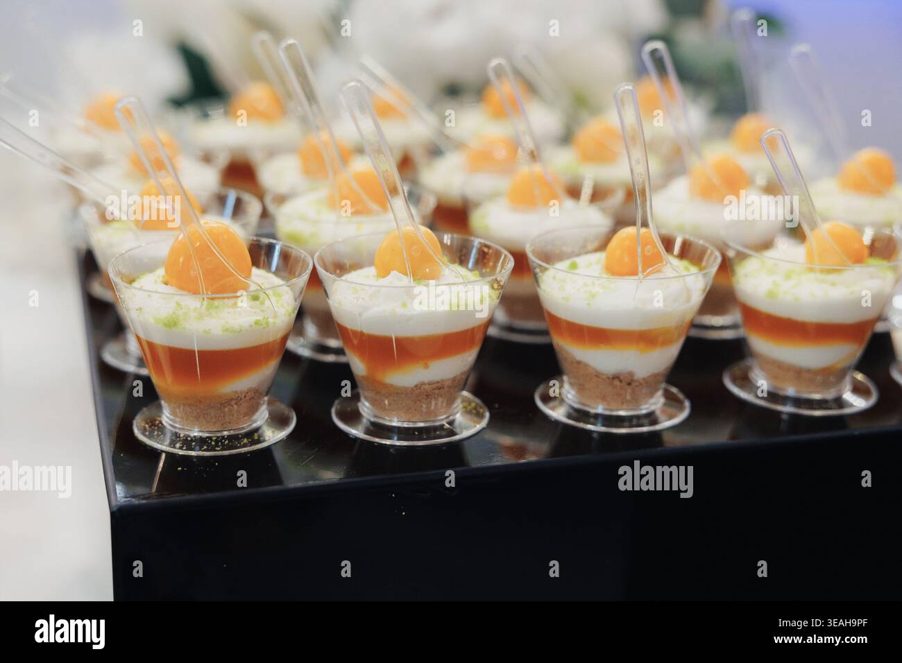 Eleganti tazze parfait a strati con mango, mousse refrigerata e strati di crema presentati in tazze trasparenti con cucchiai da degustazione, guarnizione di agrumi brillante e rumb Foto Stock