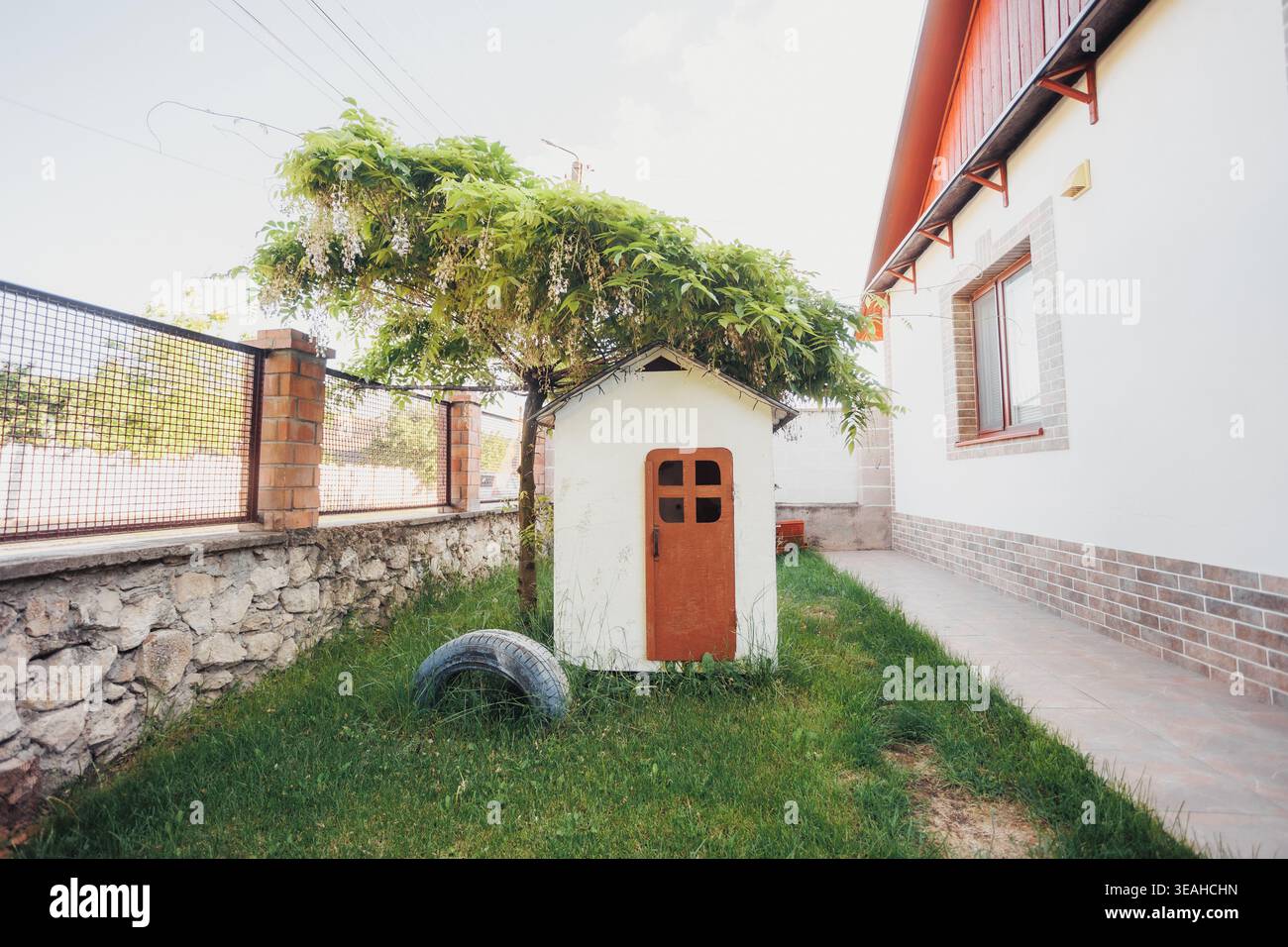 Casa giardino in miniatura con porta minuscola e vigna per arrampicata, incastonata nel prato verde accanto alla parete di pietra, ideale per giochi stravaganti per i bambini, il Giardino delle fate Foto Stock
