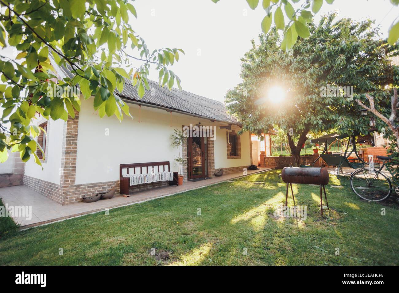 Il cortile interno illuminato dal sole con biciclette e barbecue, la calda luce dorata che filtra tra tra gli alberi sull'erba e l'atmosfera da banco evoca il tempo libero per la famiglia, picnic serale Foto Stock