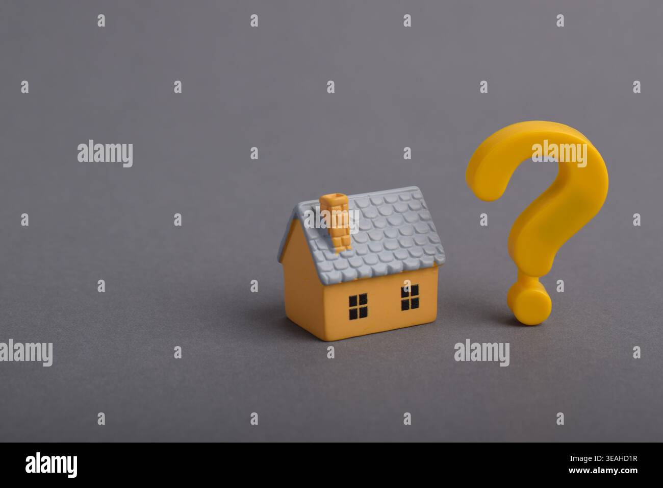 Casa in miniatura con punto interrogativo su sfondo grigio, che simboleggia la decisione immobiliare, l'incertezza immobiliare, la scelta di acquisto della casa e il rischio di investimento Foto Stock