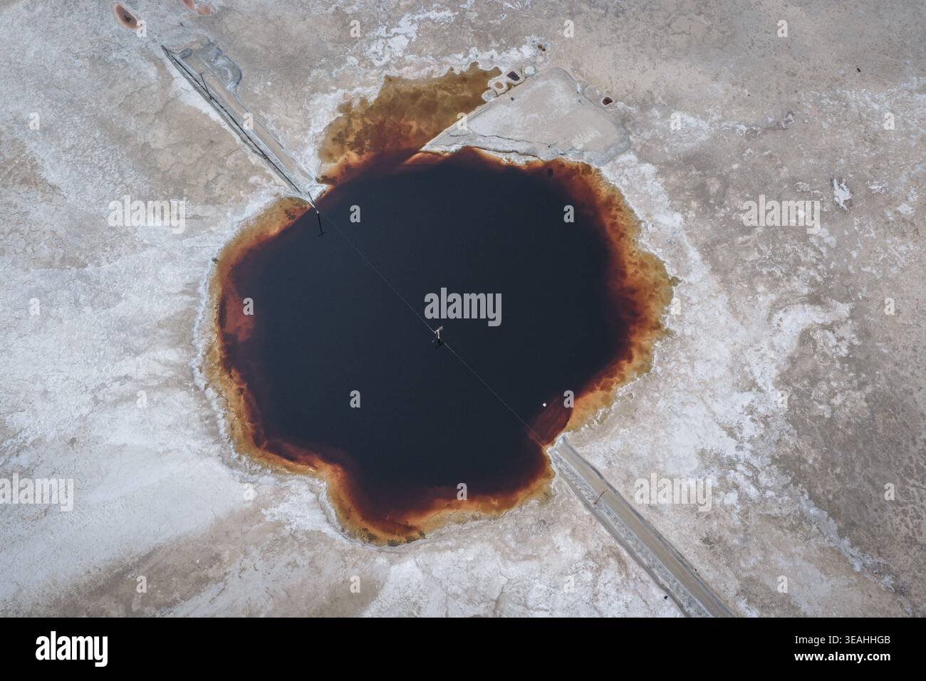 Vista aerea del lago Searles con una piscina di acqua salata scura con bordi rossastri circondata da crosta di sale bianco e una linea di attraversamento a San Bernardin Foto Stock