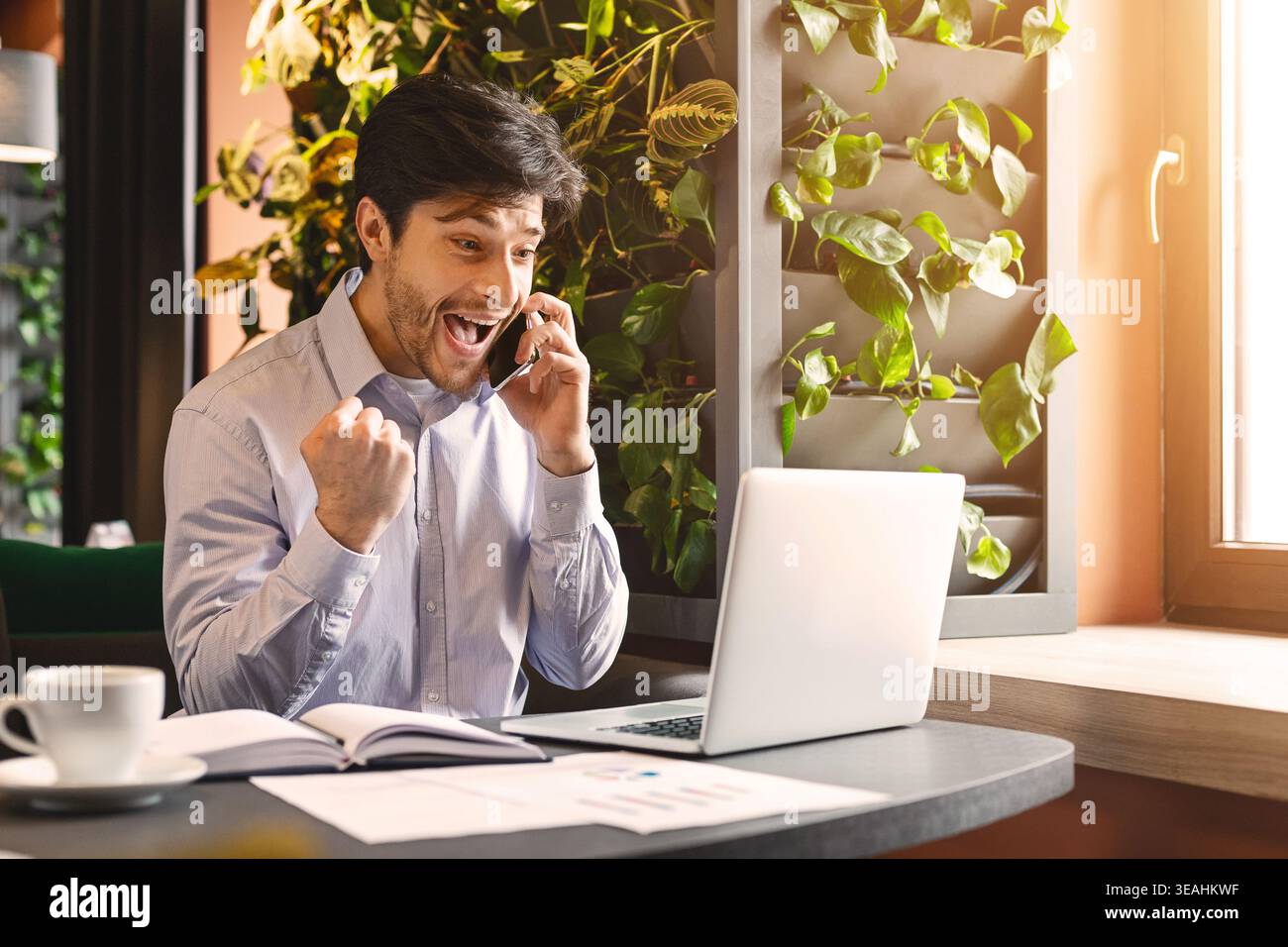 Emozionato millenaria uomo d affari con computer portatile aperto parlando al telefono Foto Stock