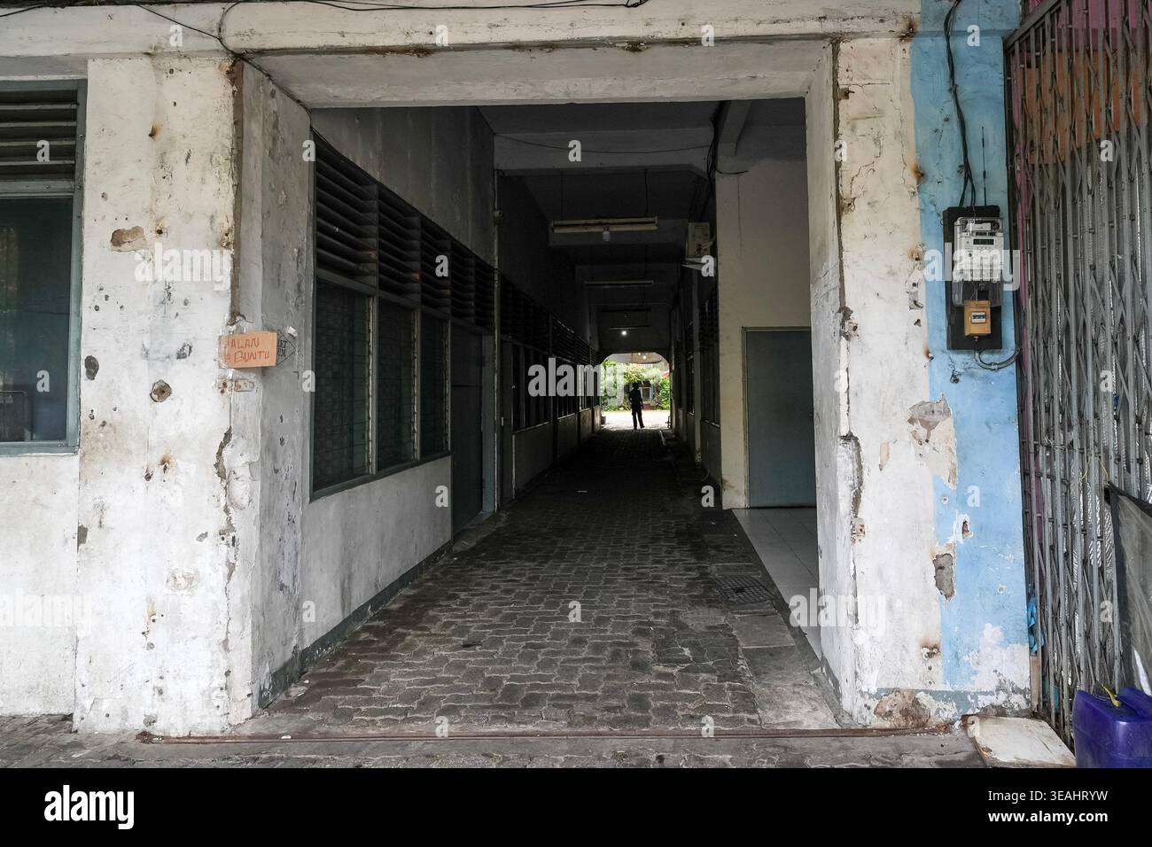 Un passaggio pedonale lungo e stretto attraverso un edificio di epoca coloniale nel centro storico di Giacarta, caratterizzato da pareti in cemento armato e da un distinto edificio Foto Stock