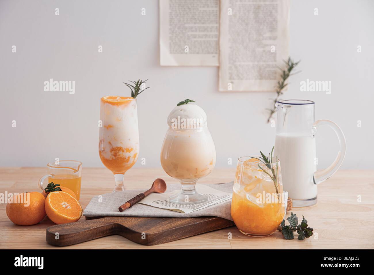 Una varietà di bicchieri e una caraffa di bevande arancioni e bianche si siedono su un tavolo di legno in una sala ben illuminata. Foto Stock