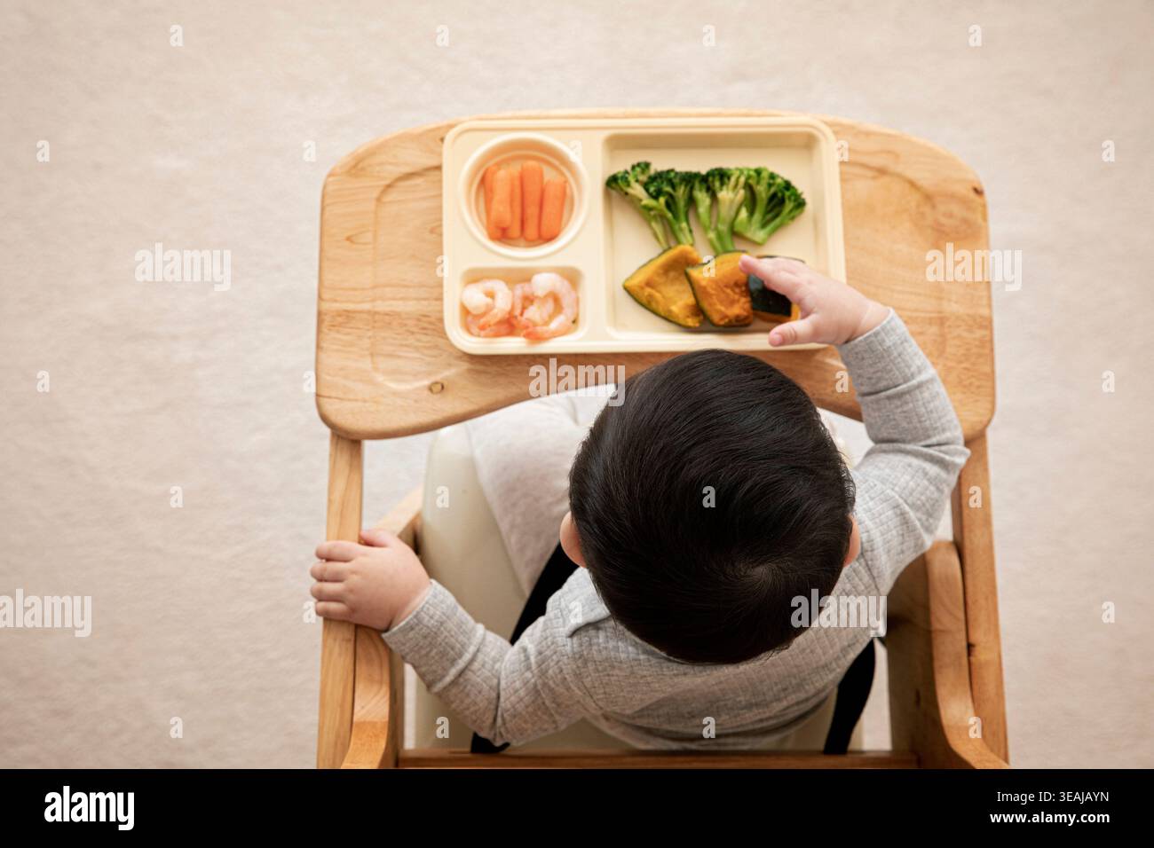 Un bambino si siede su un seggiolone e cerca un flolet di broccoli su un vassoio di cibo. Foto Stock