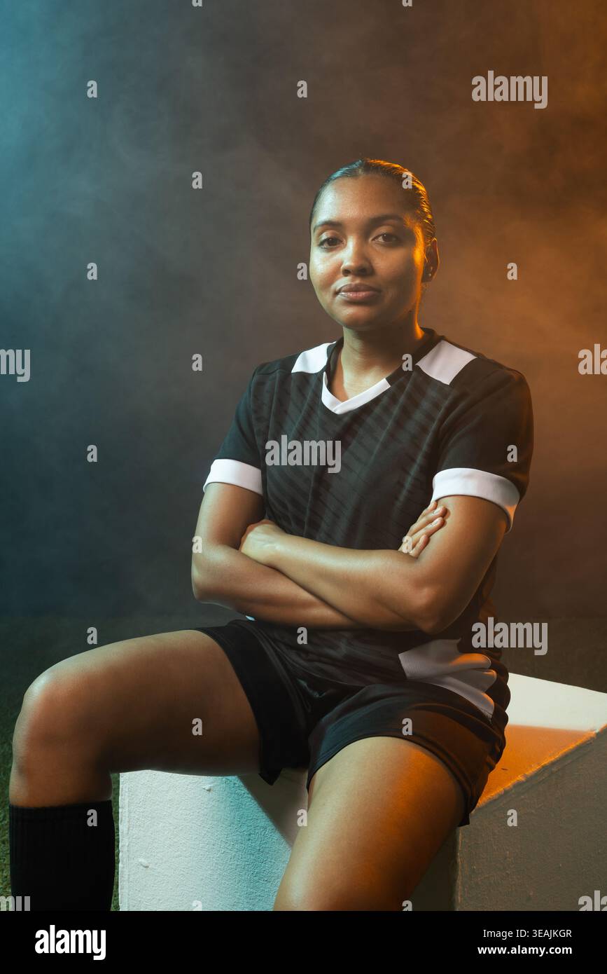 Donna seduta su un cubo bianco in studio che indossa una maglia nera, calze al ginocchio e foschia per creare sfumature Foto Stock