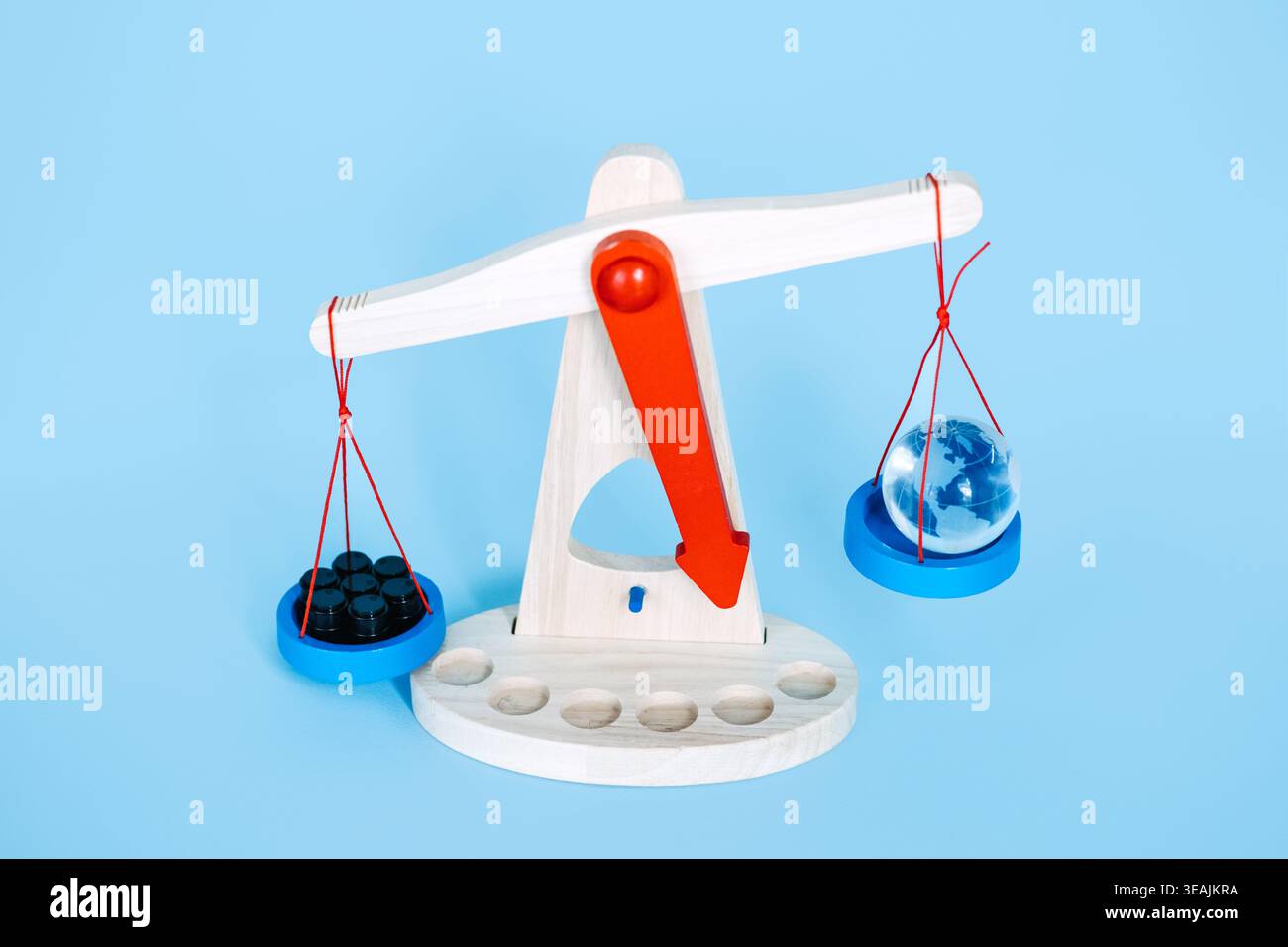 Bilance in legno che pesano piccole botti nere su globo in vetro su sfondo blu. Esaurimento globale delle risorse, dipendenza dai combustibili fossili, approvvigionamento energetico Foto Stock