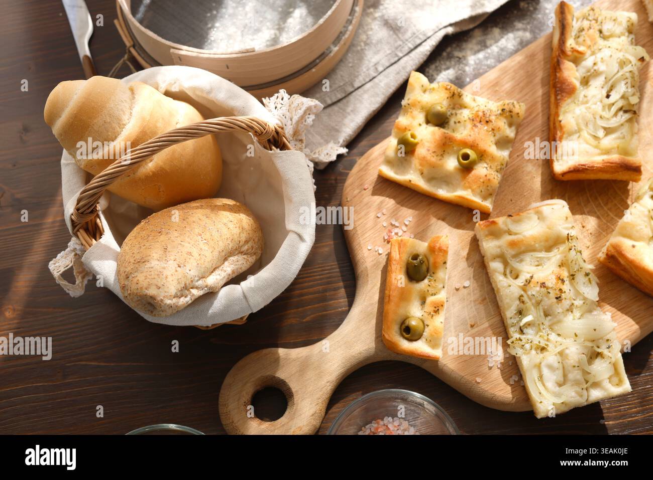 Pane italiano assortito con focaccia e olive su tavola di legno. Vista dall'alto dei prodotti da forno freschi, compresi i panini nel cestino e la focaccia affettata Foto Stock