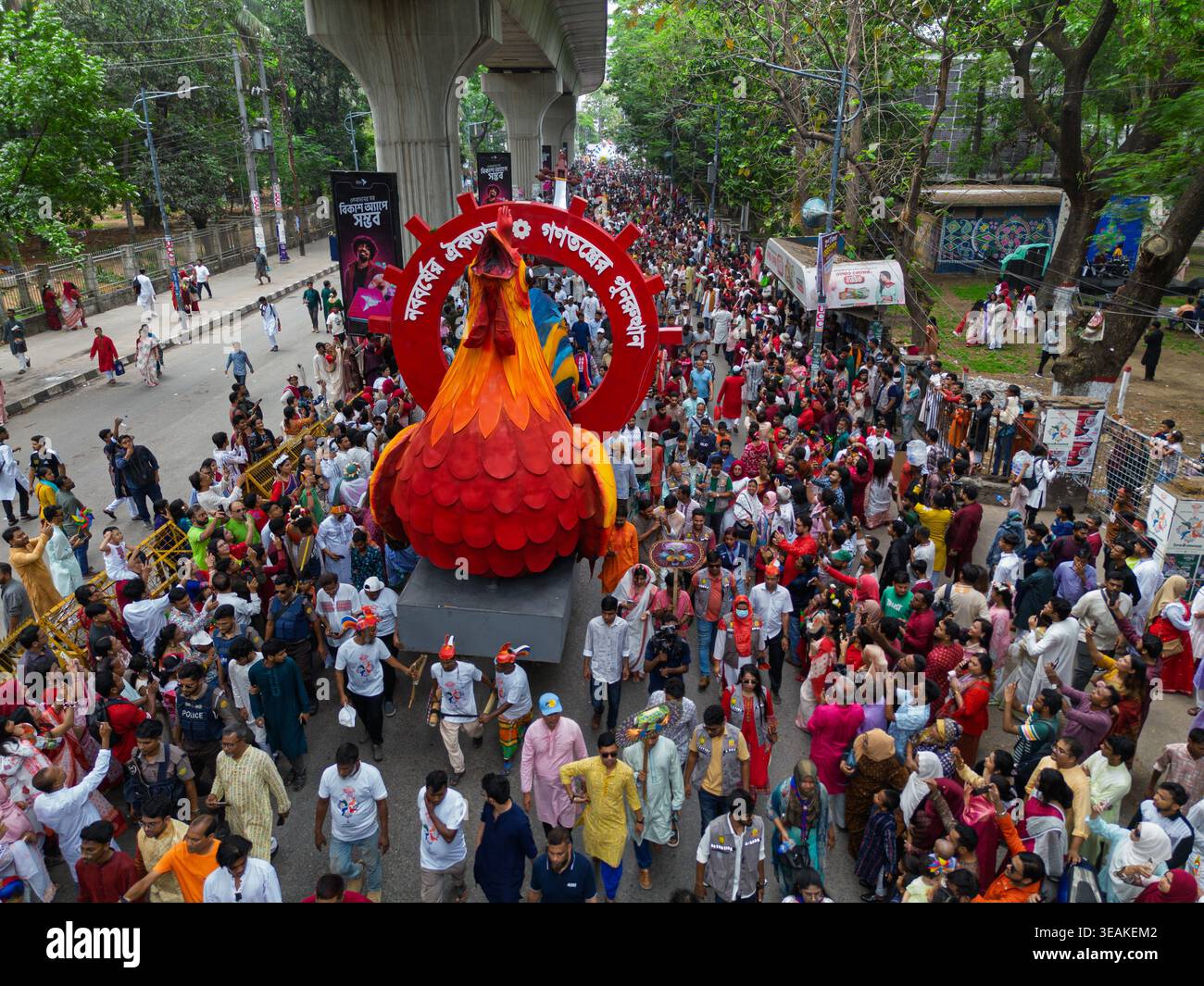 Dhaka, Bangladesh - 14 aprile 2026: Veduta aerea di una vivace processione, ricca di sfumature rosse, che scorre sotto la linea sopraelevata della metropolitana della città, creando un Foto Stock