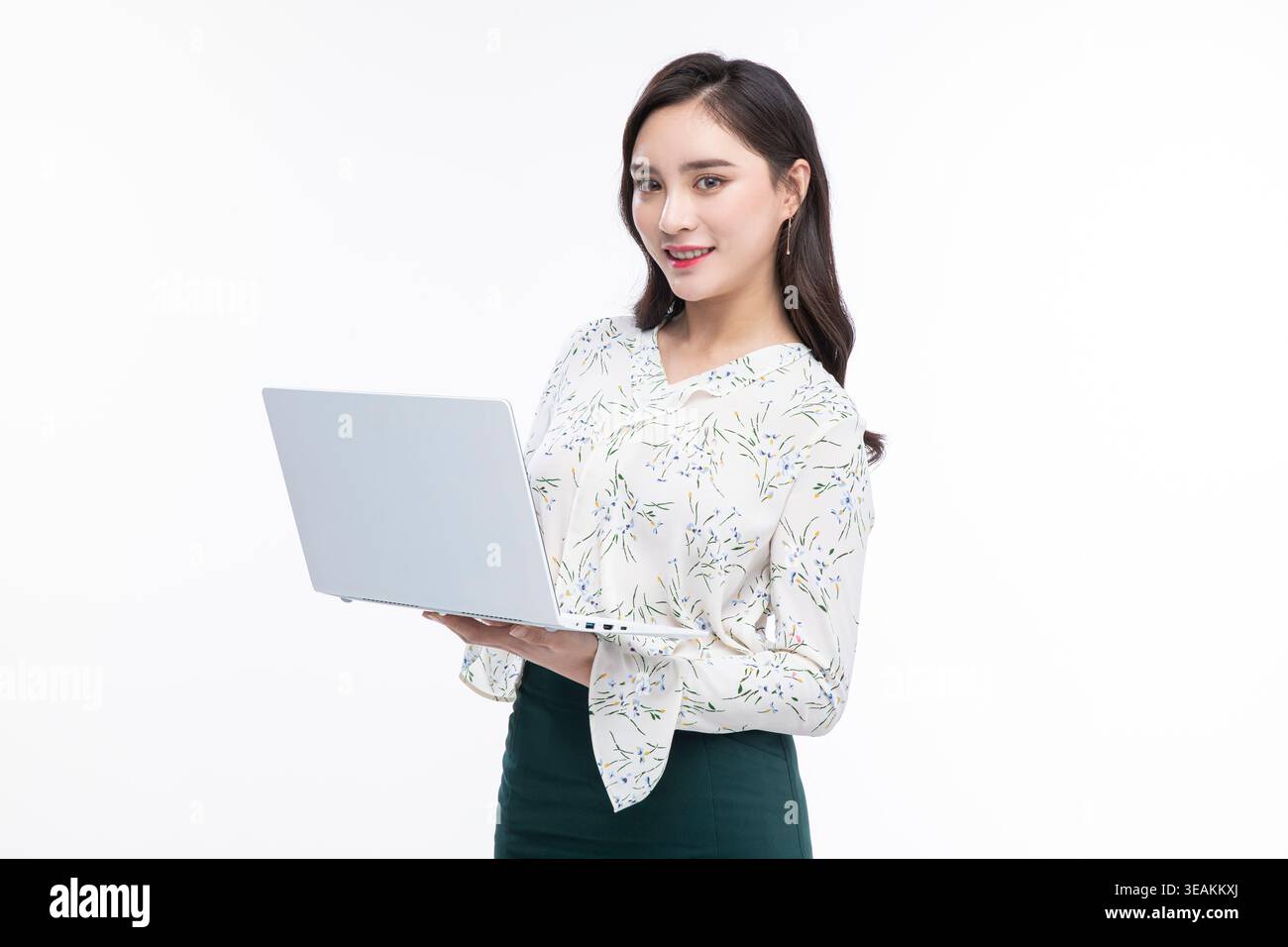 Una giovane donna con una blusa bianca e una gonna scura lavora su un laptop in una stanza luminosa e neutra. Foto Stock