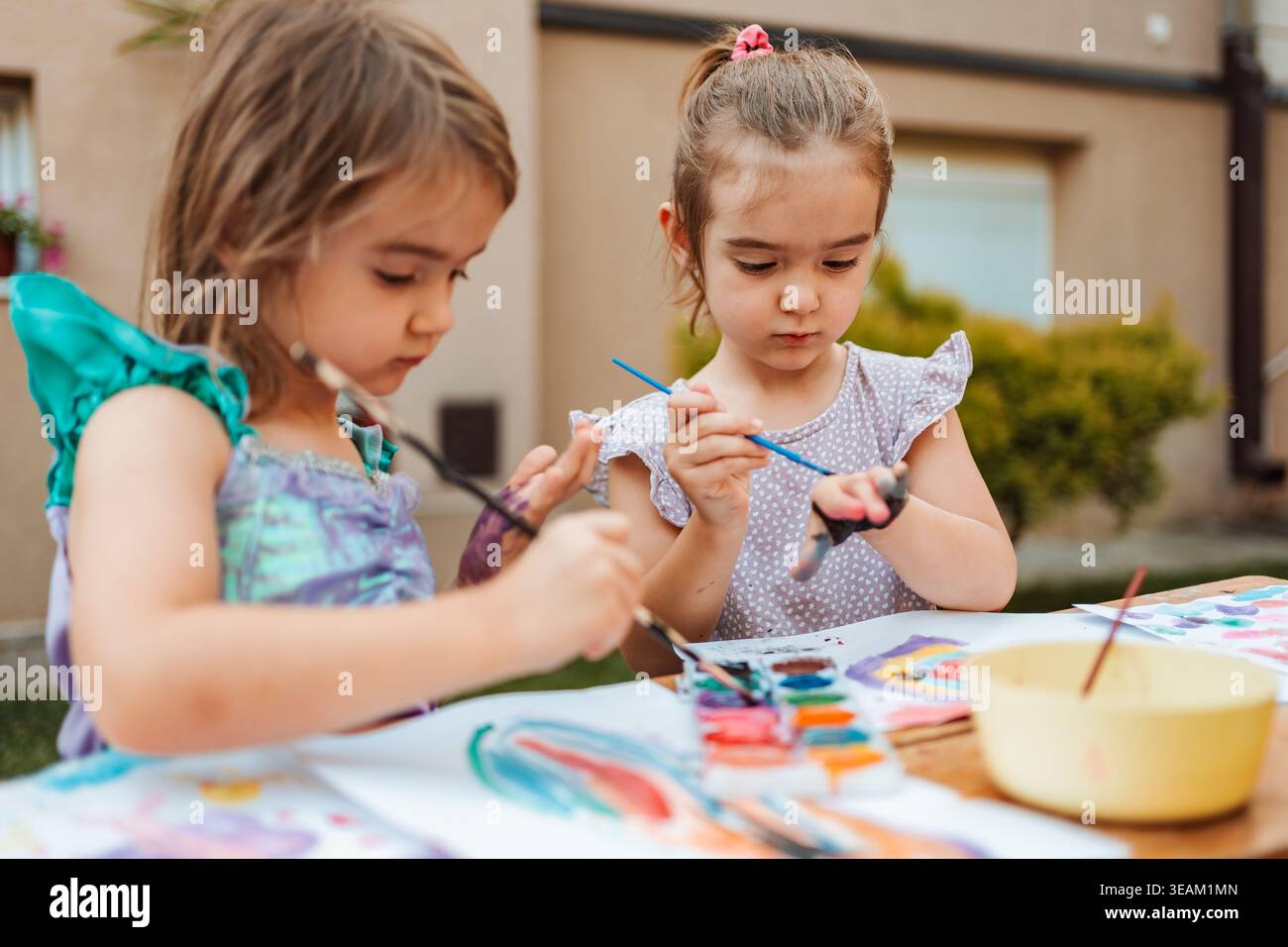 Due ragazze in età prescolare che dipingono con acquerelli nel cortile posteriore Foto Stock