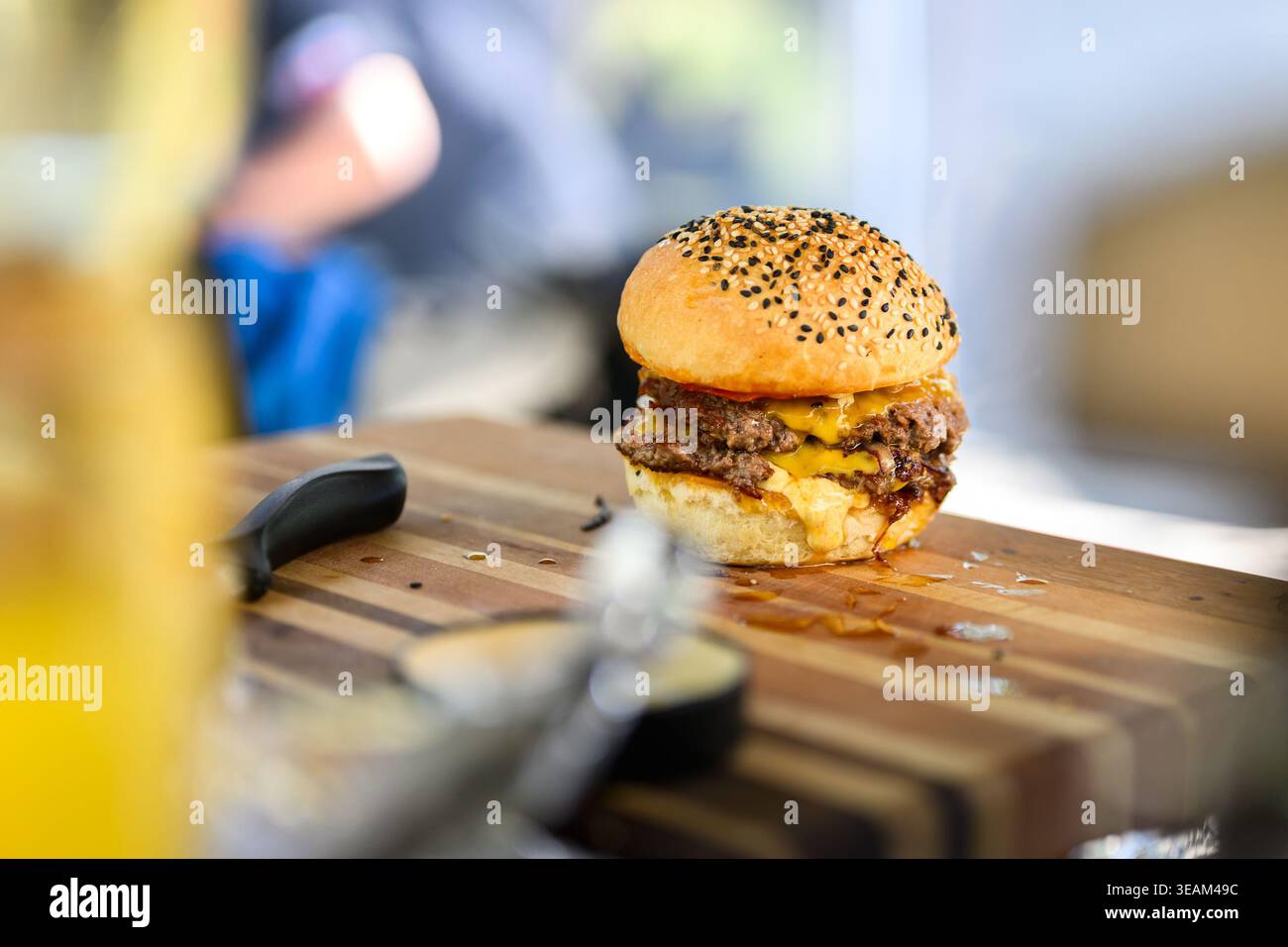 Primo piano di un cheeseburger appena preparato con polpettine di manzo doppie, formaggio fuso e panino di sesamo posto su una superficie di legno, che mostra succose Foto Stock