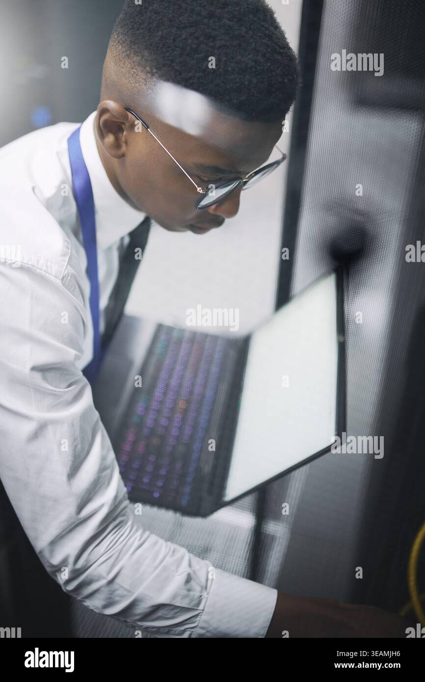 Tecnico, uomo o laptop per l'ispezione della sala server per la diagnostica, l'aggiornamento hardware o versioni successive. Ingegnere IT, persona nera e tecnologia nel data center per Foto Stock