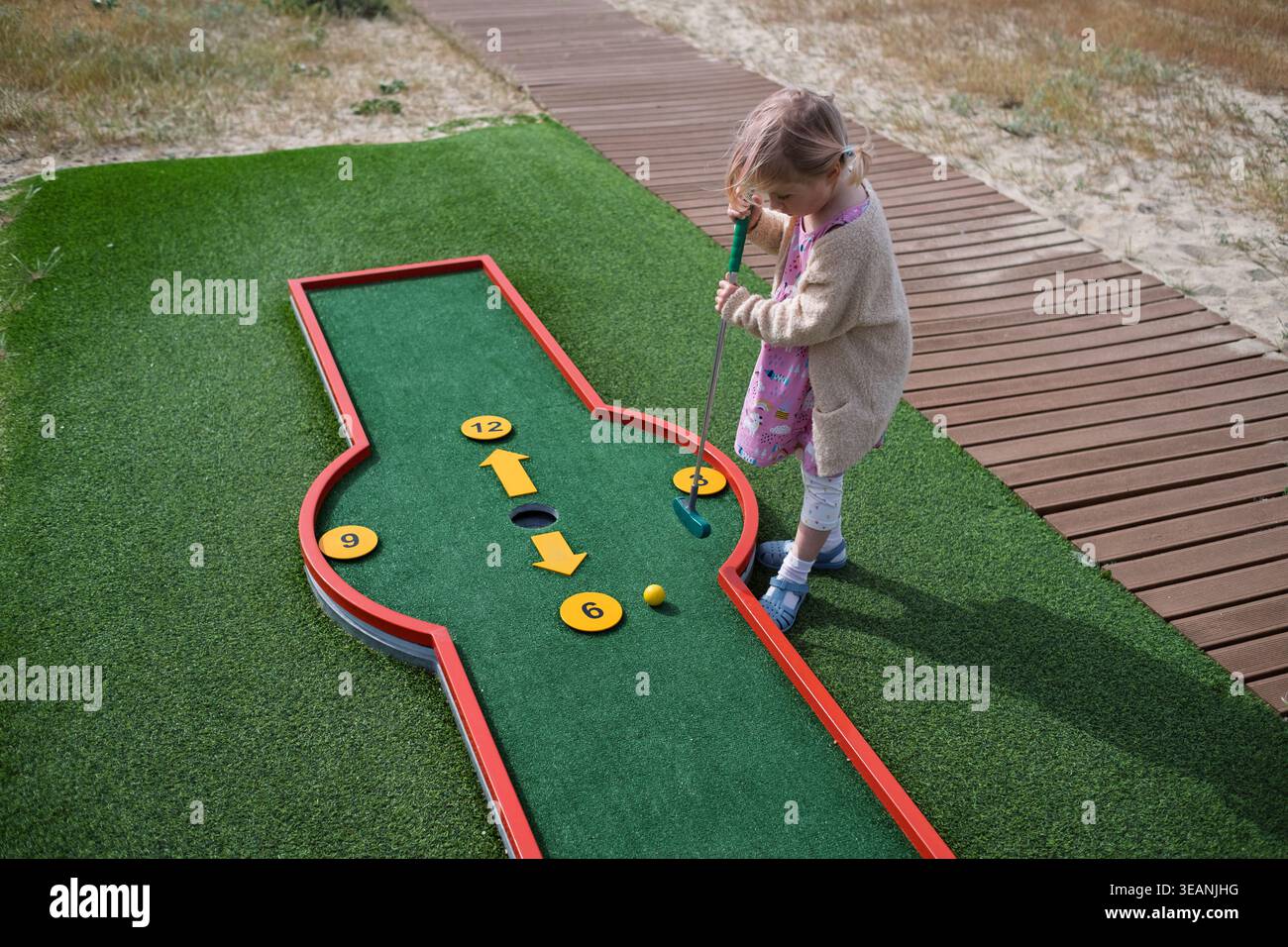 Infanzia spensierata: Blonde Girl gode di una divertente giornata di minigolf in città Foto Stock