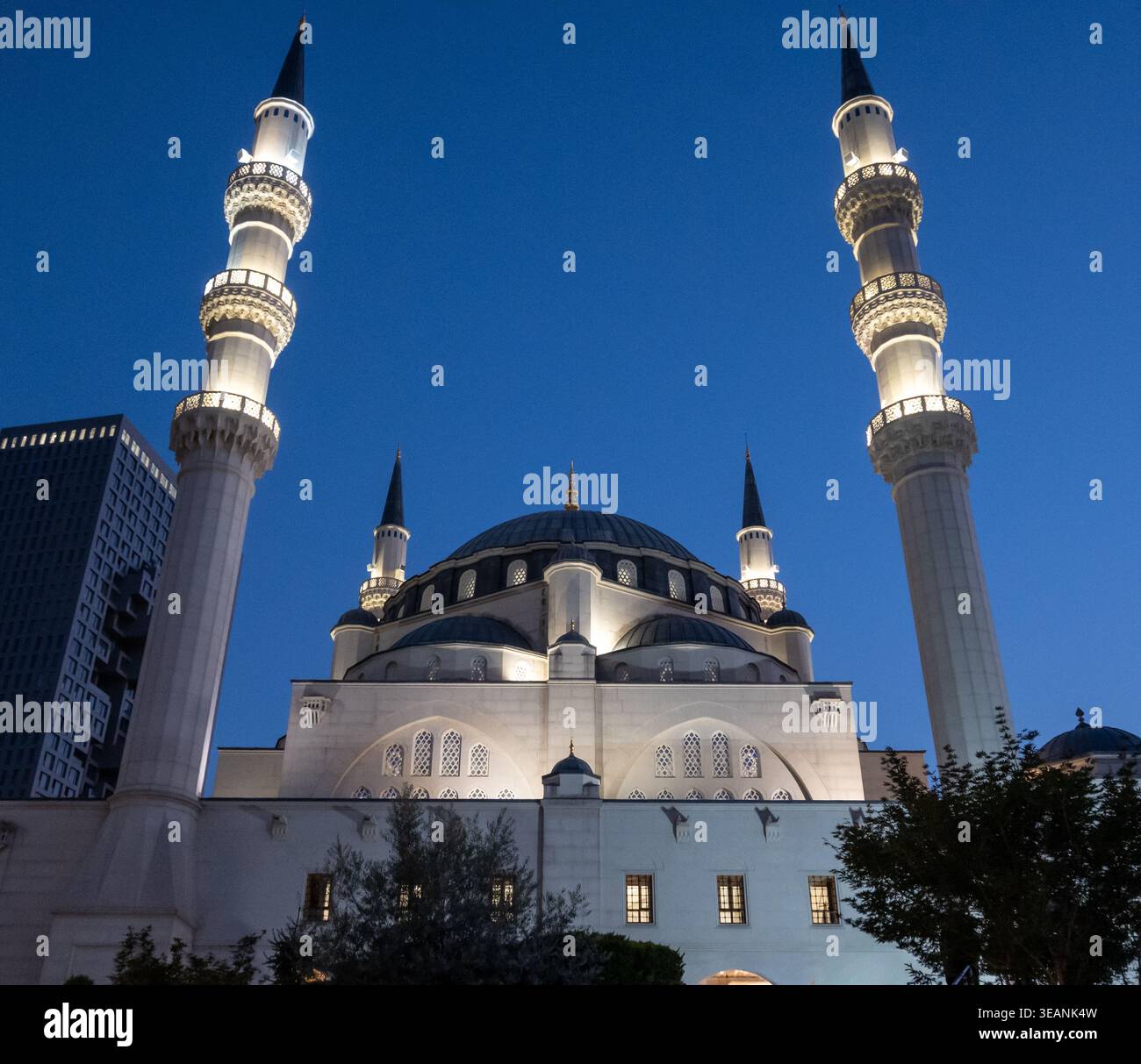 Moschea di Namazgah a Tirana con minareti illuminati e cupola contro un cielo notturno blu profondo. Foto Stock