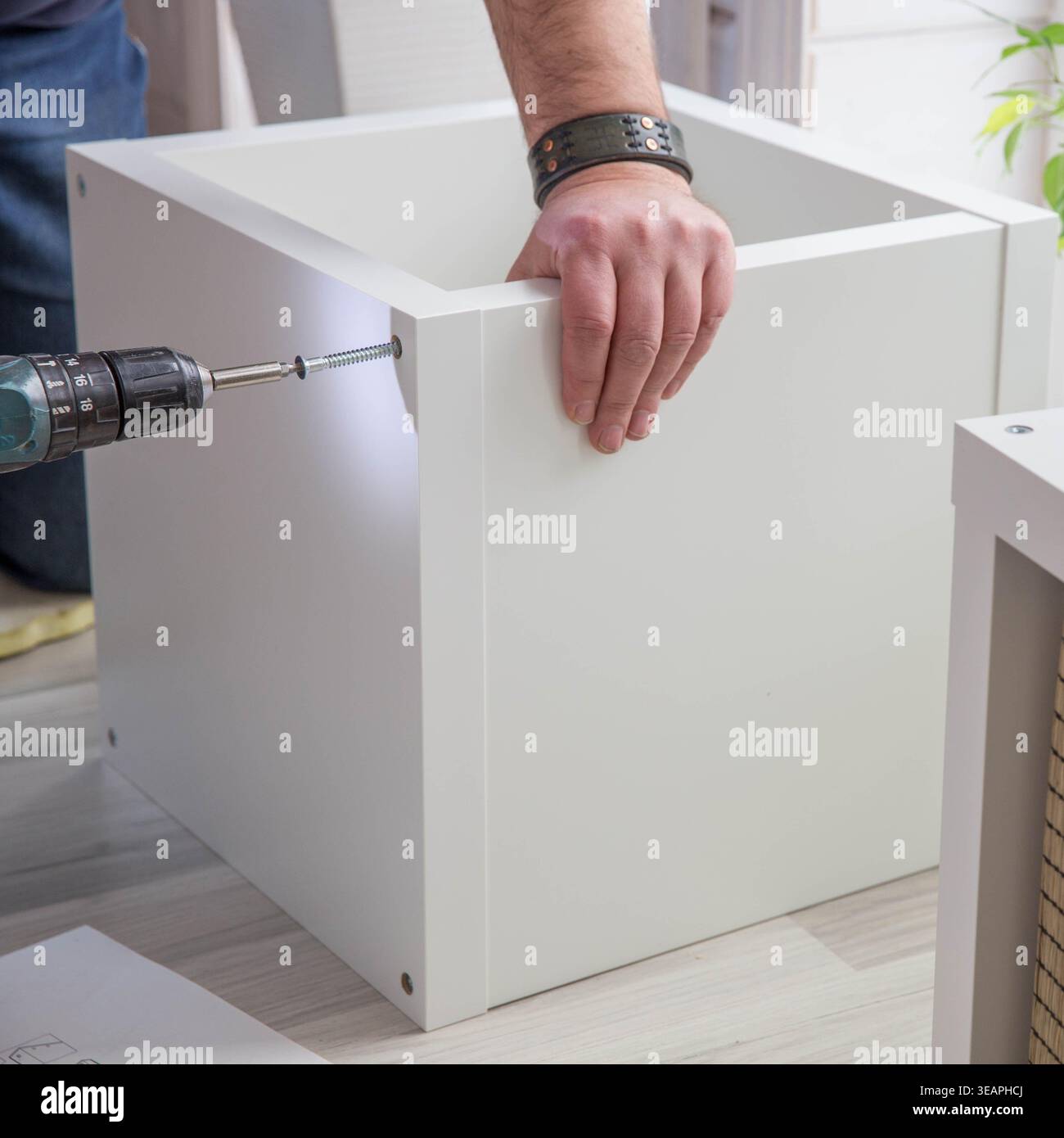 Uomo che assembla armadietto bianco per mobili con trapano a batteria, primo piano del pannello di fissaggio manuale con vite durante l'installazione di mobili per la casa, interni fai da te Foto Stock