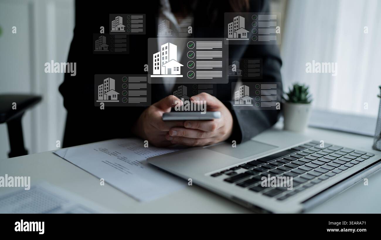 Un professionista aziendale è impegnato nel lavoro utilizzando uno smartphone e un computer portatile in un ufficio moderno. La grafica per la gestione immobiliare fornisce un formato digitale Foto Stock