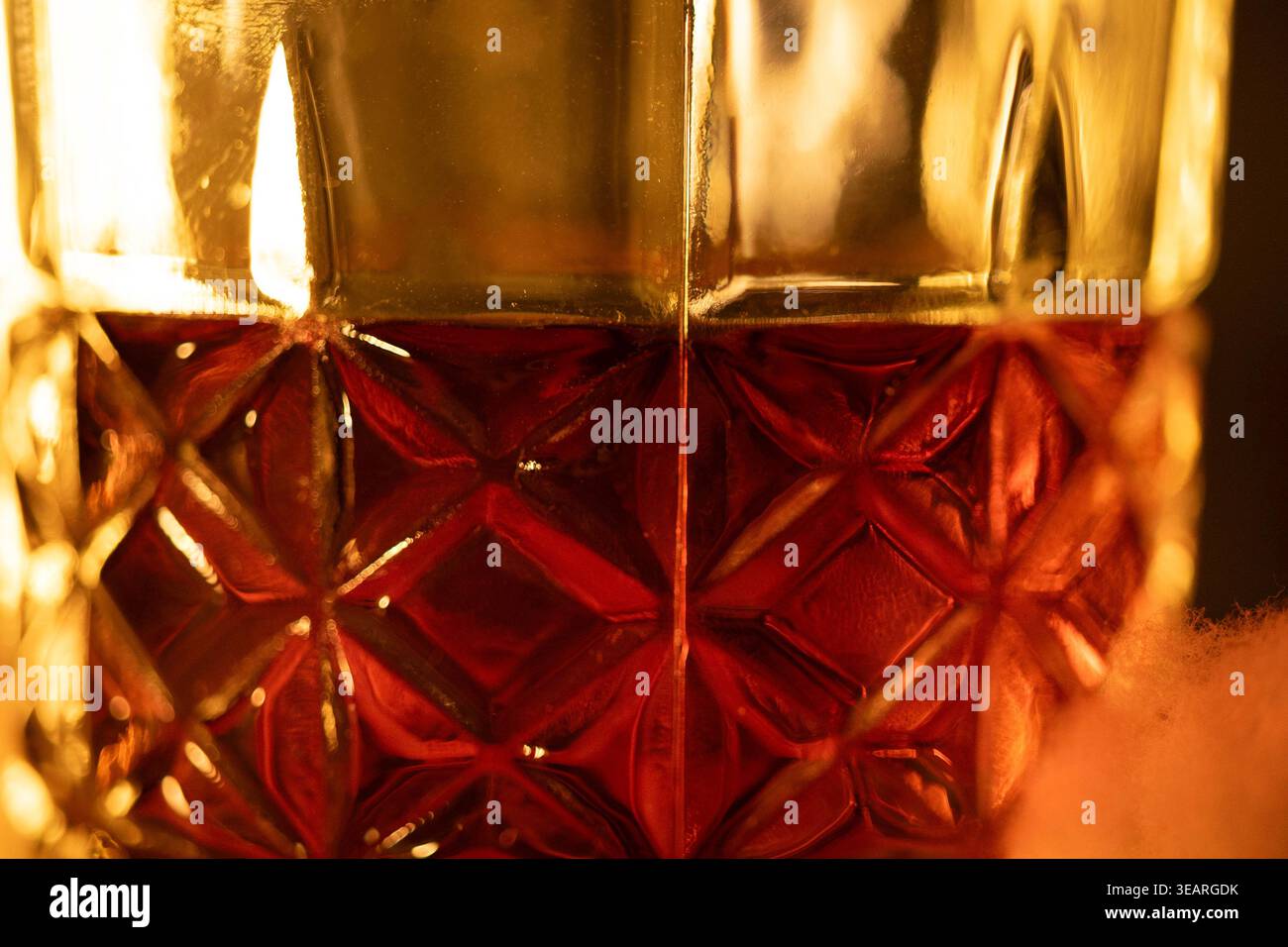 Un bicchiere testurizzato riempito di whisky color ambra sotto una luce calda che mette in risalto i riflessi. Concetti: Un'atmosfera elegante associata al lusso Foto Stock