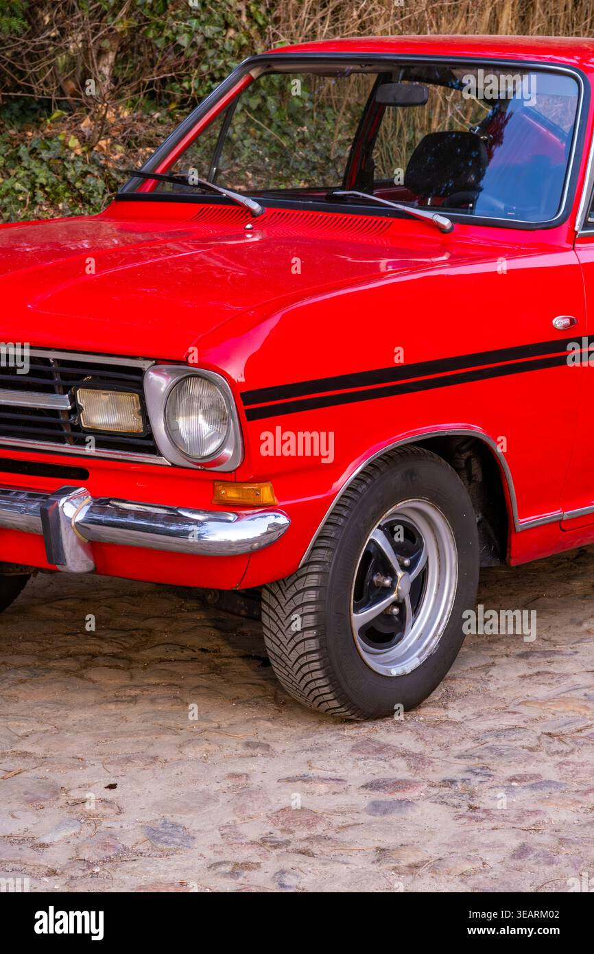 Un'auto d'epoca di colore rosso brillante è parcheggiata su una strada acciottolata, che mostra il suo classico stile frontale. Paraurti cromato, fari rotondi e Foto Stock