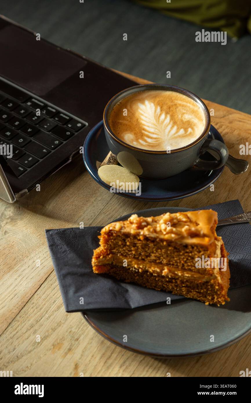 Un computer portatile su un tavolo con un caffè e una fetta di torta alle noci Foto Stock