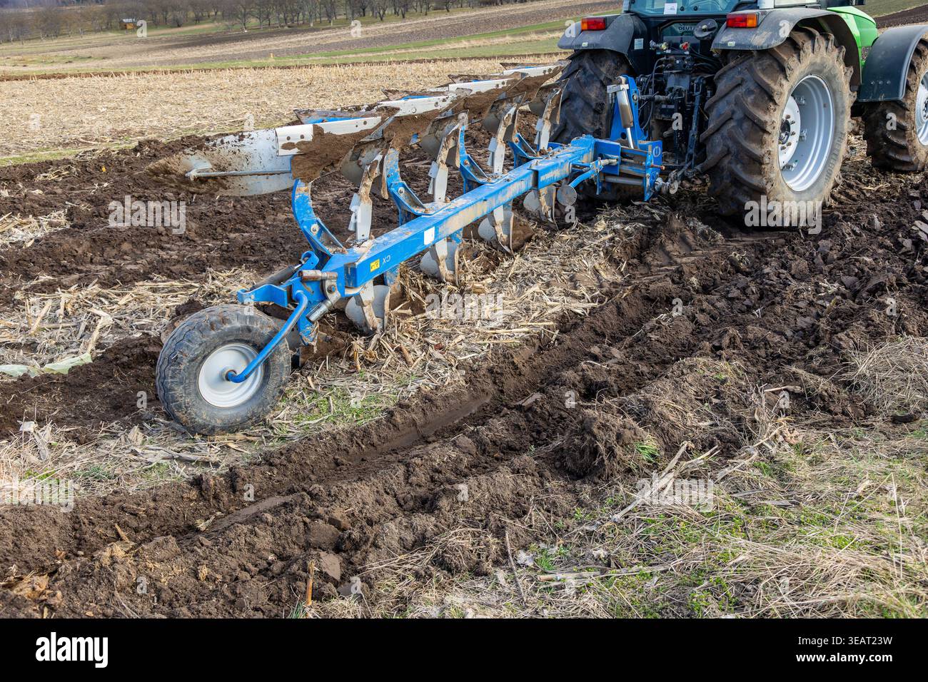Prima piano di un trattore che ara un campo agricolo con un aratro a più solchi durante la preparazione del terreno in primavera per la coltivazione delle colture Foto Stock