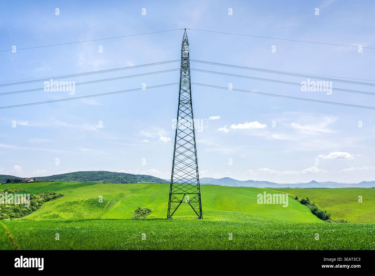 La torre della linea elettrica ad alta tensione si trova in un lussureggiante campo verde in Toscana. Infrastrutture moderne in un paesaggio rurale primaverile vicino a Volterra Foto Stock