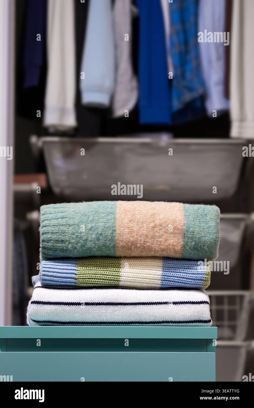 Pullover impilati in blu pastello, beige, bianco e blu pastello. Armadio aperto con appendiabiti e cassetti sullo sfondo. Concetto di organizzazione guardaroba, SEA Foto Stock
