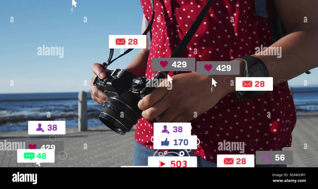 Reflex digitale regolabile, donna con la parte superiore a pois rossa e jeans che incorniciano la passerella sul mare con cuori fluttuanti Foto Stock