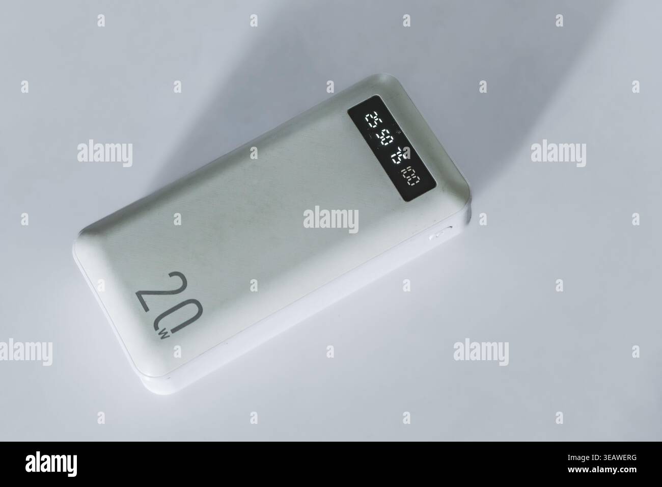Una vista dall'alto verso il basso di un elegante power Bank portatile bianco appoggiato su una superficie bianca semplice. Il dispositivo è dotato di un testo di 20 W. Foto Stock
