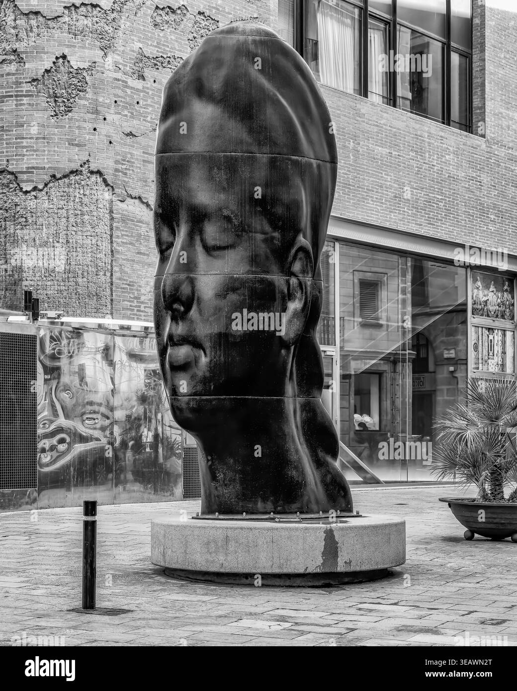 Grande scultura moderna a testa nera di Jaume Plensa in una piazza urbana pubblica circondata da architettura classica in mattoni e moderna in vetro Foto Stock