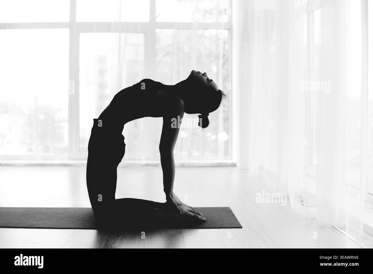 Silhouette di una persona che pratica yoga in un tranquillo spazio interno al tramonto Foto Stock