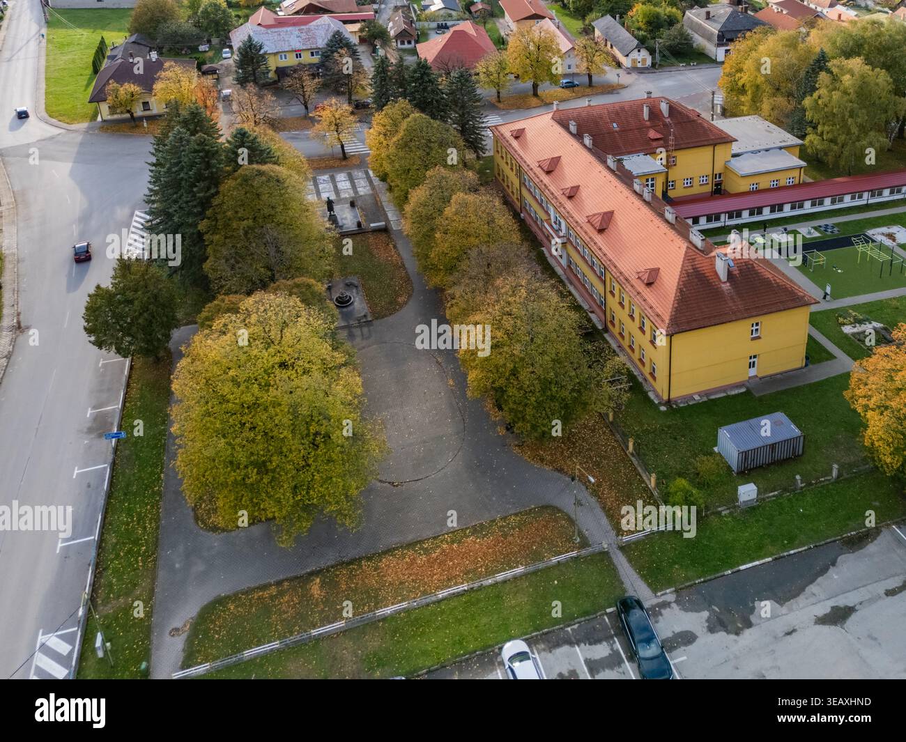 Vista aerea di un edificio giallo vibrante con un suggestivo tetto di piastrelle rosse, annidato tra un arazzo di alberi verdi e dorati d'autunno, Mosovce, Zilina R. Foto Stock