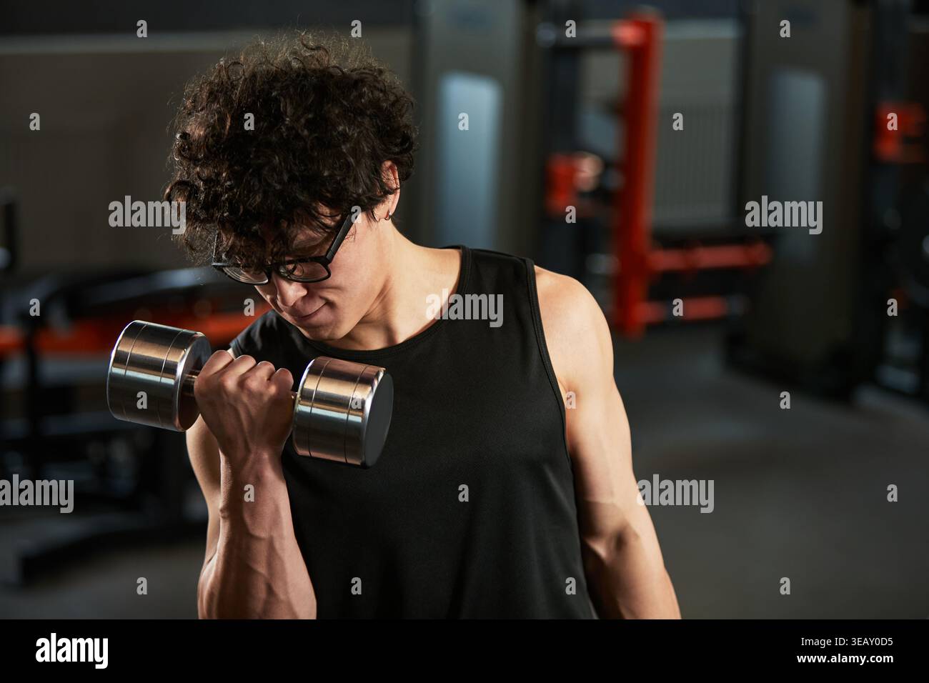 Giovane uomo adulto che si esercita con il manubrio, eseguendo ricci bicipali durante l'allenamento di forza in palestra. Adatto per fitness marketing, programmi di allenamento, promozioni di allenamento personale Foto Stock