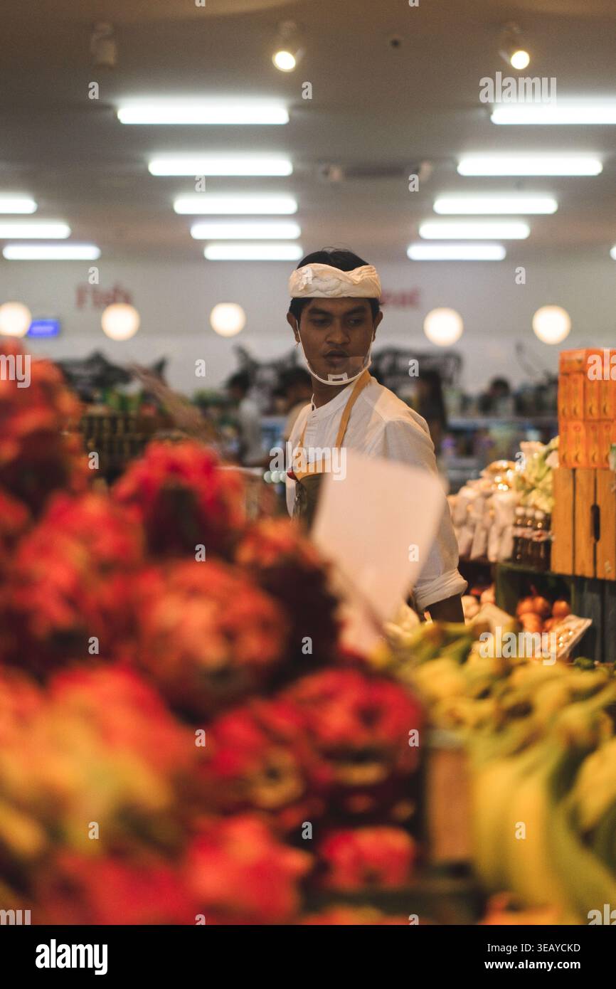 Operaio del mercato balinese con archetto tradizionale nella sezione frutta, Bali Foto Stock