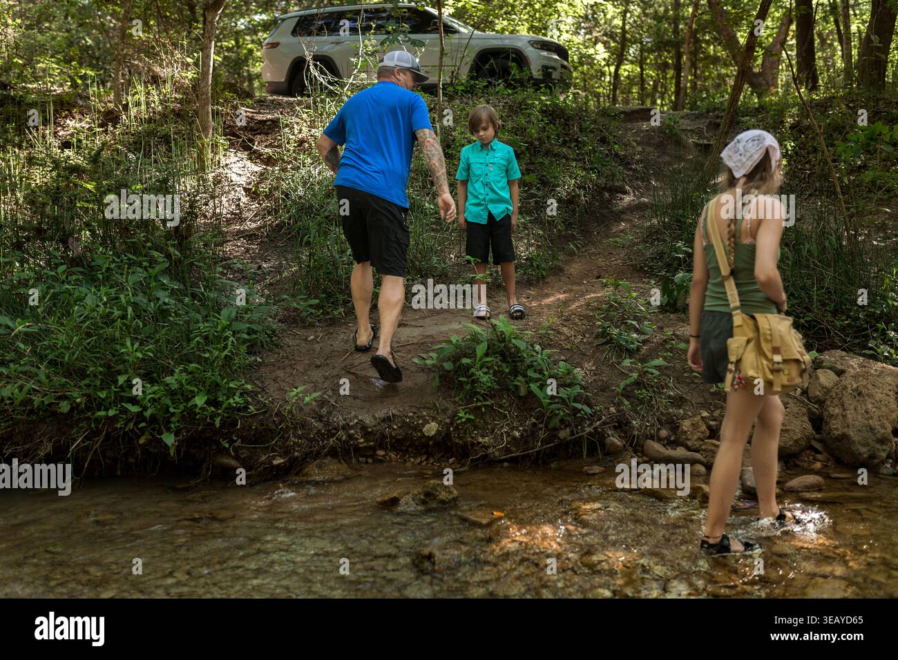 Famiglia che attraversa il torrente poco profondo sul sentiero della foresta vicino al SUV parcheggiato Foto Stock