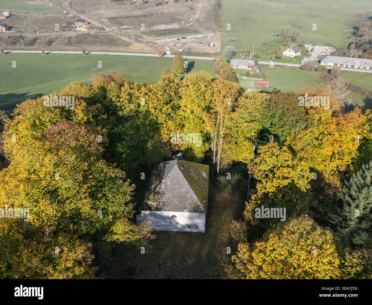 Vista aerea della chiesa con un tetto grigio circondato da alberi con foglie gialle, Sebeslavce, Blatnica, Zilinsky kraj, Slovacchia. Foto Stock