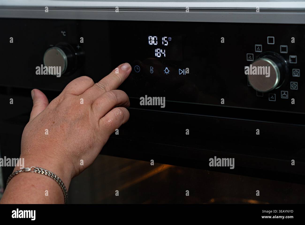 Vista ravvicinata di una mano che aziona il pannello di controllo digitale di un forno moderno, regolando la temperatura e le impostazioni di cottura per la precisione culinaria Foto Stock