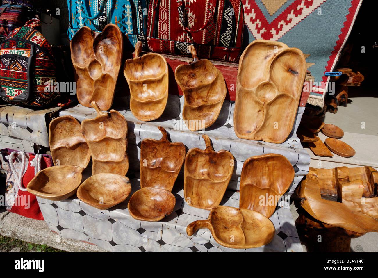 Vassoi e piatti in legno fatti a mano con forme organiche esposti in un mercato di souvenir all'aperto con borse in tessuto a motivi tradizionali Foto Stock