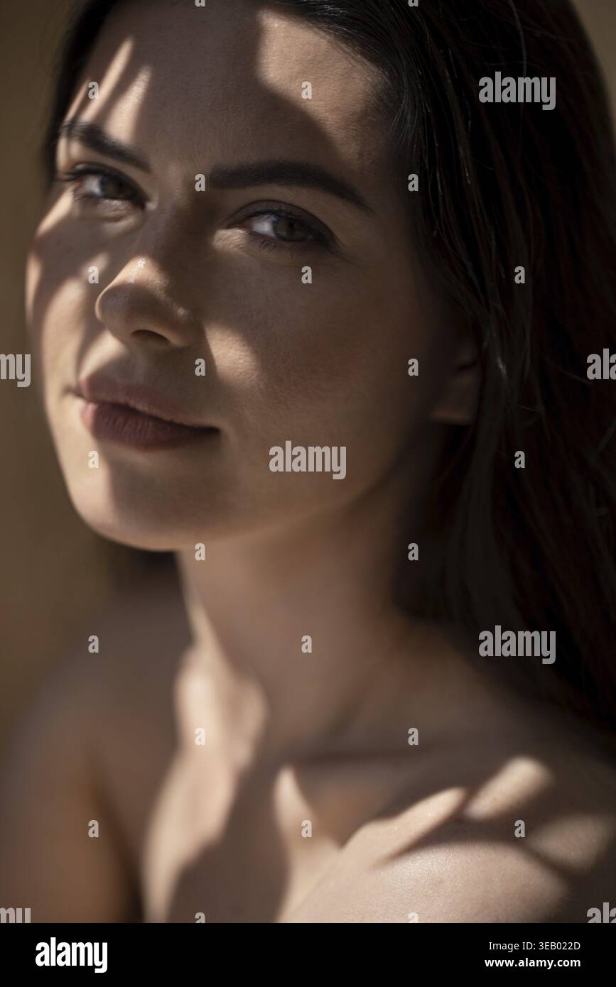 Ritratto di una giovane donna dai lunghi capelli scuri, illuminata dalla luce del giorno, che disegna delicate ombre sul viso e incarna bellezza e tranquillità Foto Stock