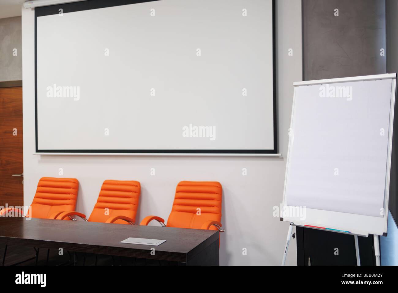 Sala conferenze con proiettore, lavagna a fogli mobili e sedie arancioni pronte per la presentazione Foto Stock