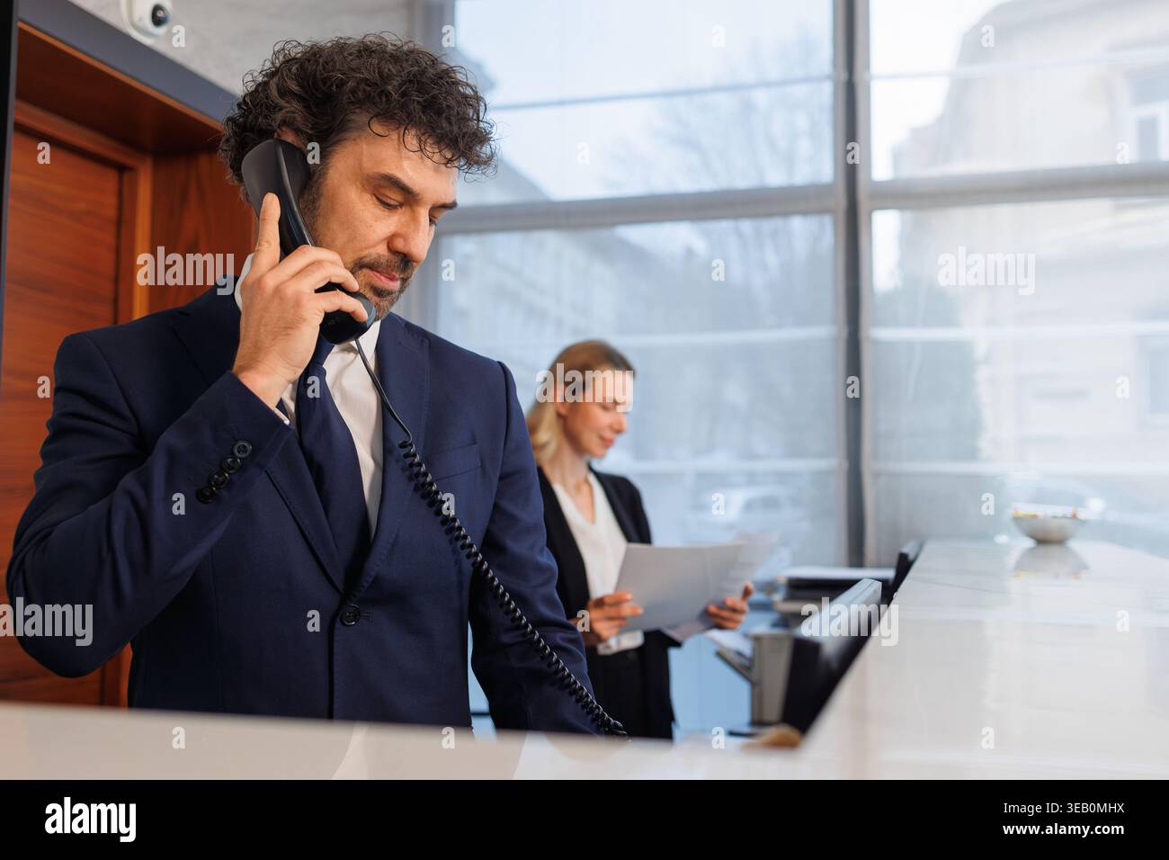 La receptionist parla al telefono dell'ufficio con una dipendente in background Foto Stock