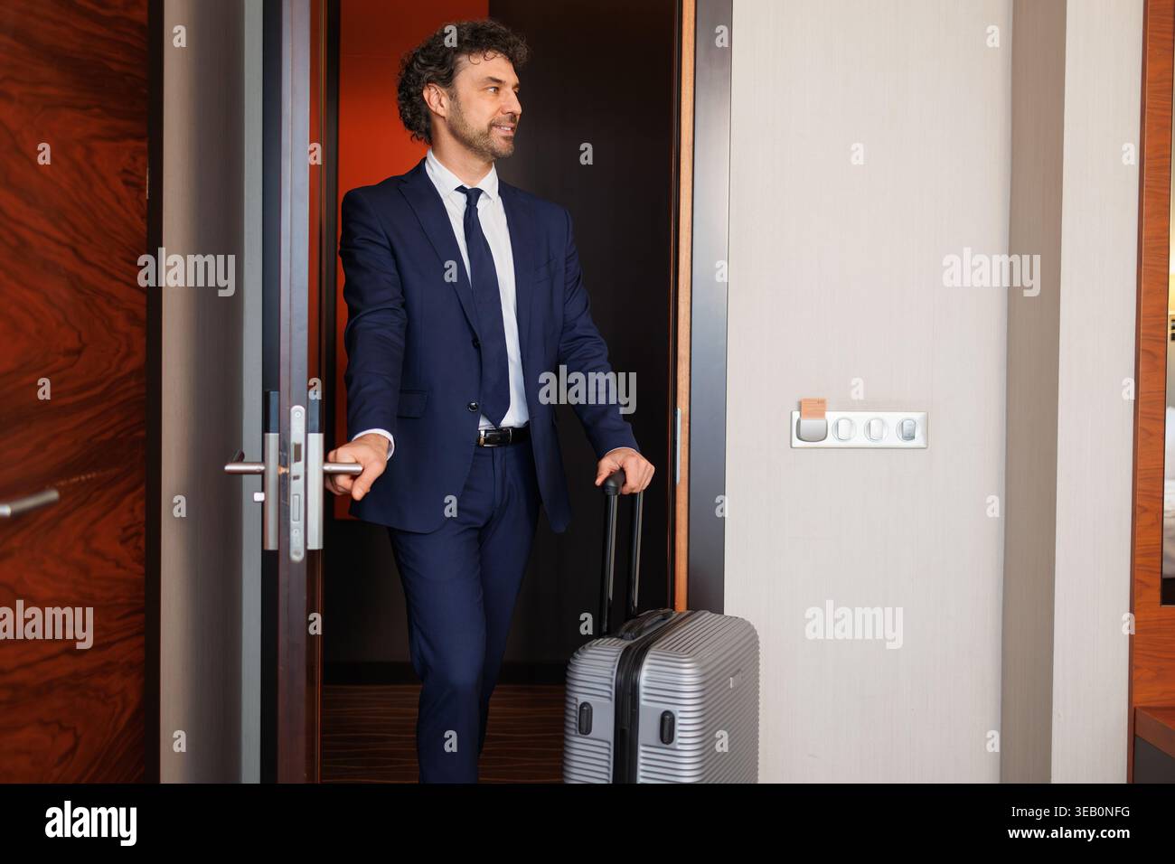 Uomo d'affari professionale che entra nella suite dell'hotel con bagagli a rotelle Foto Stock
