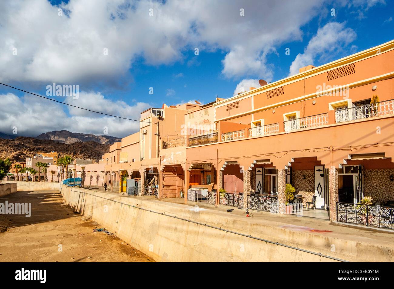 Tafraoute, strada cittadina con piccoli stabilimenti e negozi allineati su un lato, alberi con fogliame verde e cielo blu appaiono sullo sfondo, in th Foto Stock