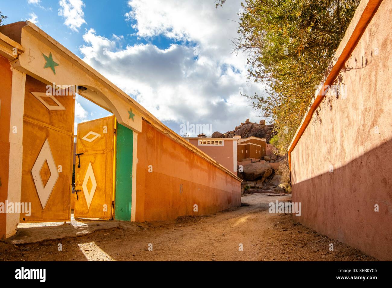 Una strada sterrata, la strada è delimitata da alte mura, che delimitano proprietà o edifici tradizionali, e accanto ad essa si trova un grande cancello aperto pai Foto Stock