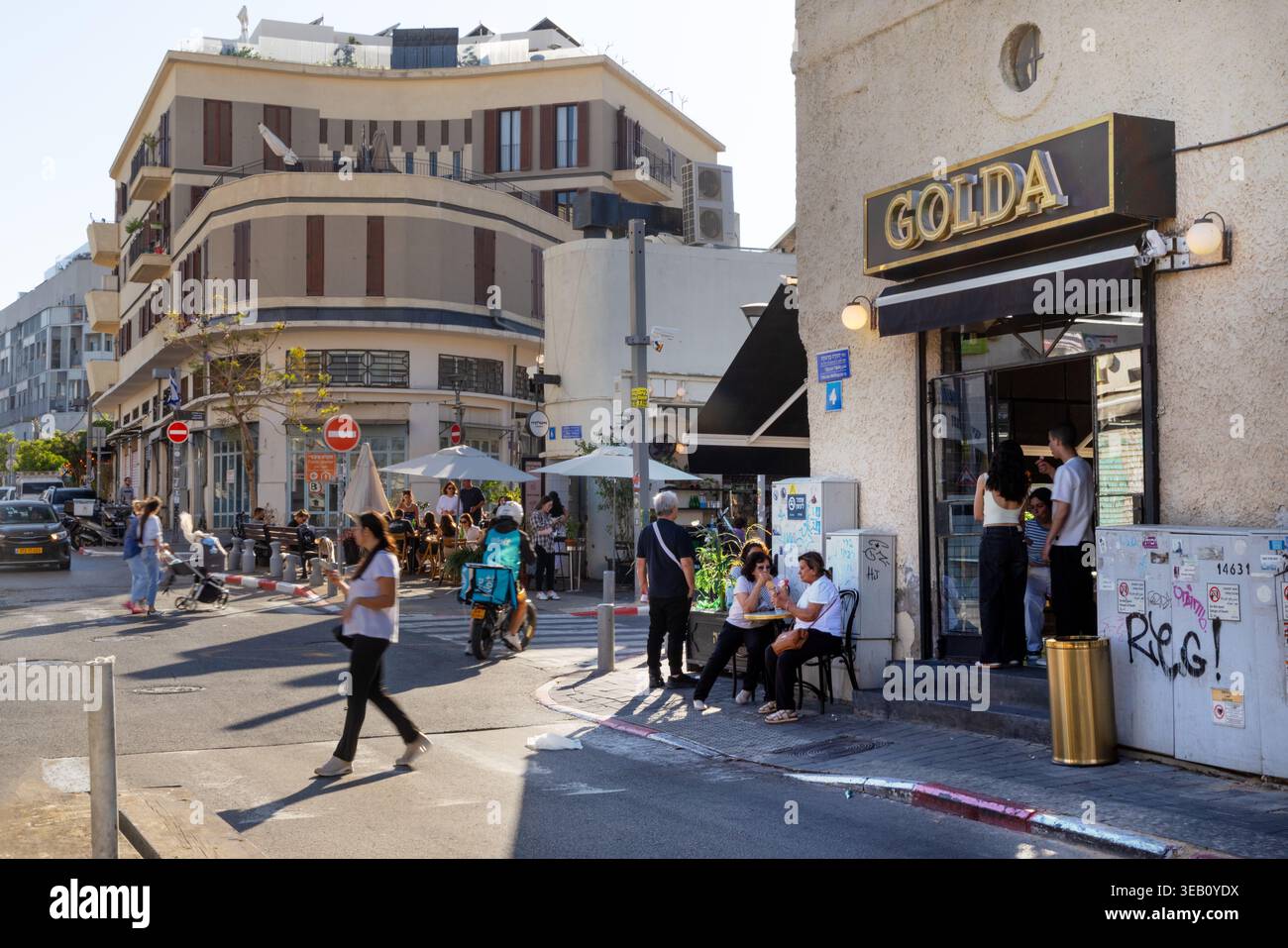 Israele, Tel Aviv, 22 aprile 2026. I pedoni camminano su una strada soleggiata vicino alla famosa gelateria Golda nella Vecchia Giaffa. Le persone si rilassano ai tavoli del marciapiede mentre la vita urbana prospera in questa zona storica Foto Stock